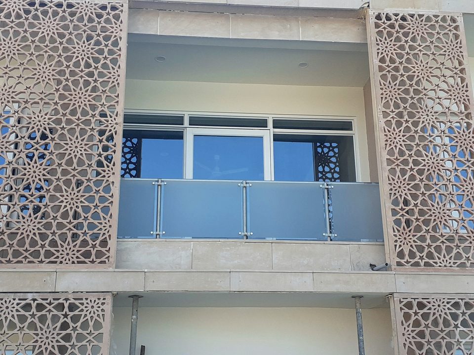 A perforated jaali screen set against a glass balcony railing, combining two packages on one elevation.
